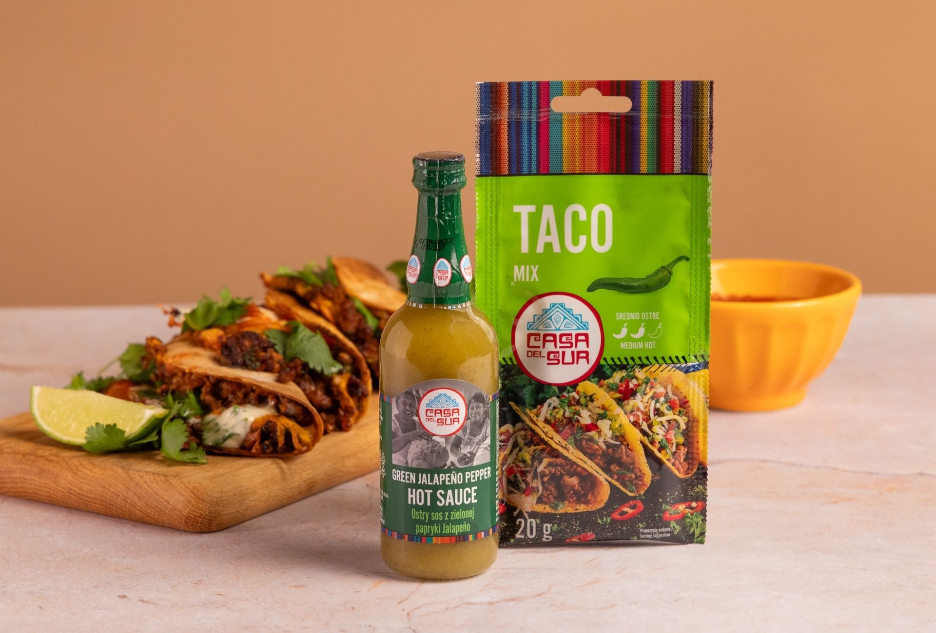 Zapiekane tacos z wołowiną, serem i kolendrą na drewnianej desce, obok sosu Green Jalapeño oraz przyprawy Taco Mix Casa del Sur.